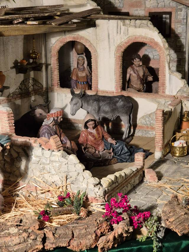 Representación detallada de un belén navideño con figuras humanas y un burro en un entorno arquitectónico antiguo.