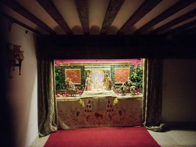 Altar religioso decorado con flores, imágenes sagradas y objetos de adoración en una sala con techo de vigas de madera.