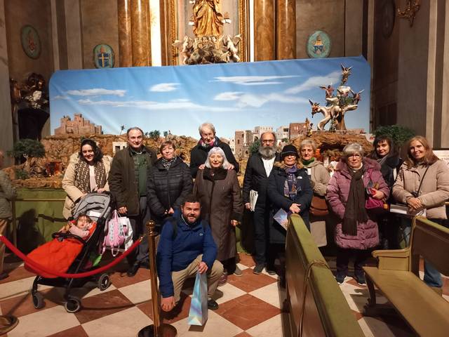 Un grupo de personas sonriendo frente a un nacimiento de tamaño grande en una iglesia.