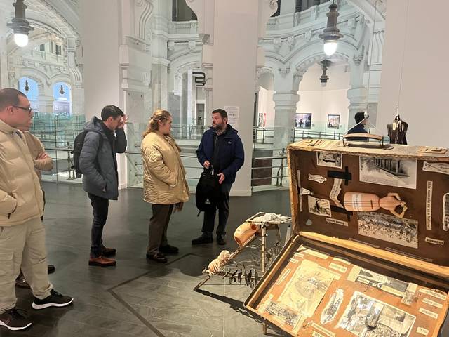 Personas observando un maletín con objetos y esculturas pequeñas en el interior de un museo.