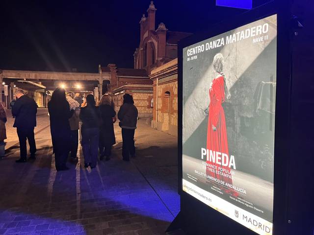 Una multitud se agrupa en la entrada de un centro cultural en una noche oscura, frente a un cartel que anuncia un evento de danza.