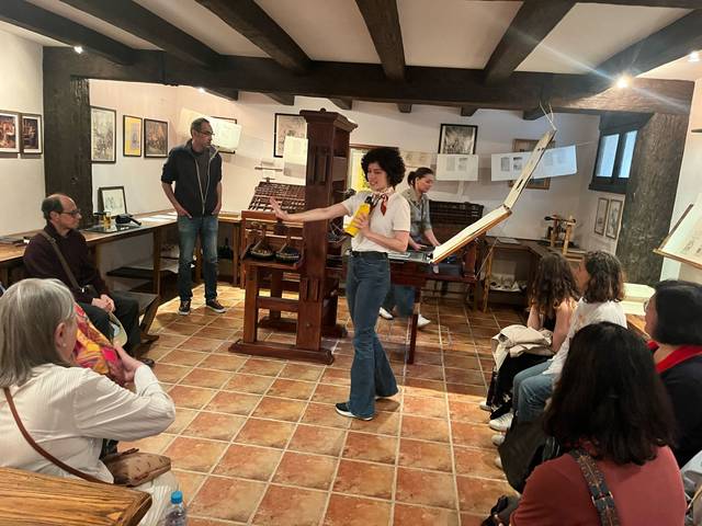 Una mujer está explicando algo a un grupo de personas en un taller de impresión.