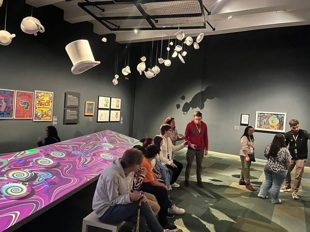 Un grupo de personas observa una exposición artística en una sala decorada con elementos surrealistas.
