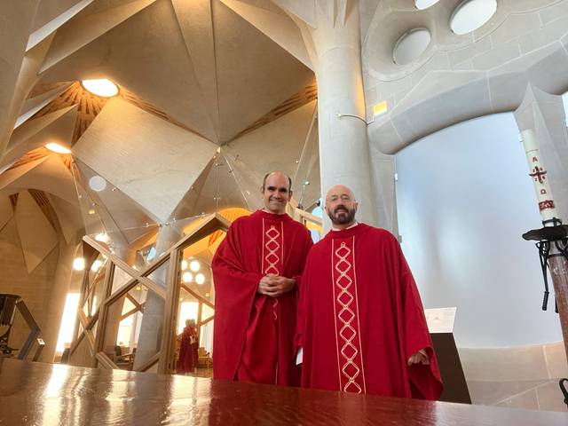 Dos hombres vestidos con ropas rojas posean en un interior moderno y arquitectónicamente innovador.