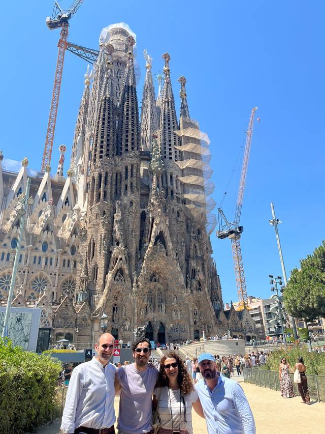 Un grupo de cuatro personas posando frente a la Sagrada Familia en Barcelona bajo un cielo azul.