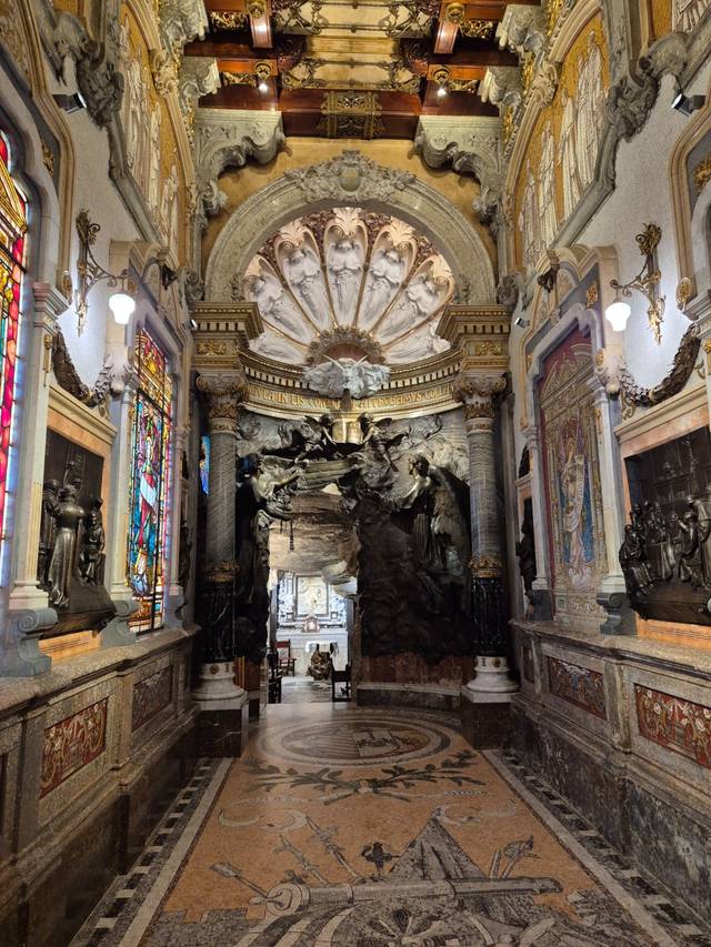 Una majestuosa sala con un elaborado techo, vitrales coloridos y esculturas en las paredes.
