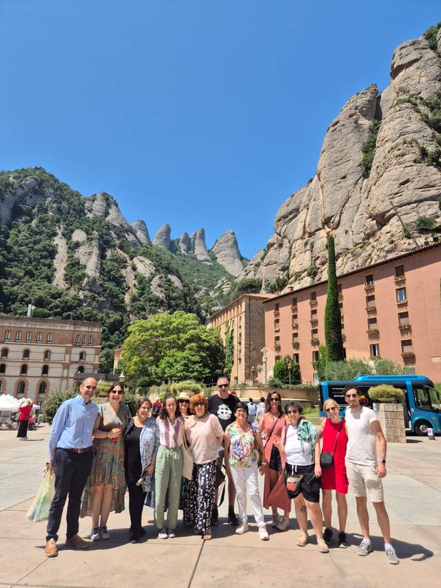 Un grupo de personas sonrientes posando frente a montañas y edificios en un día soleado.