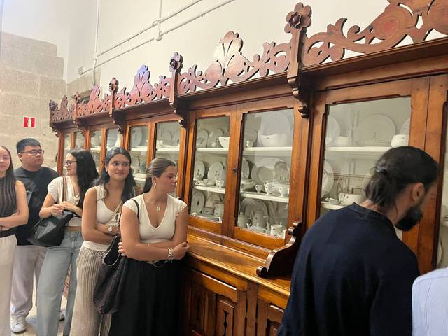 Un grupo de personas hace fila frente a una vitrina de madera que exhibe vajilla de cerámica.