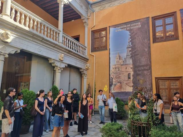 Un grupo de personas se encuentra en un patio admiring la arquitectura y un mural en el Torreón de Lozoya en Segovia.