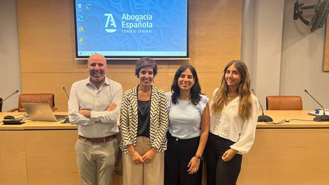 Cuatro personas sonrientes posan juntas en un ambiente profesional frente a una pantalla con el logo de Abogacía Española.