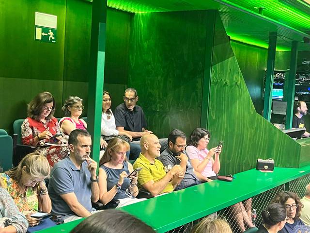 Un grupo de personas sentadas en un entorno verde, concentradas en sus teléfonos móviles.