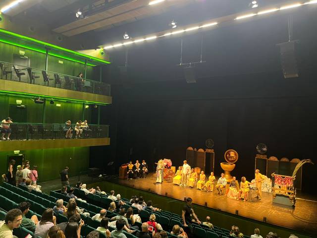 Una representación teatral con actores vestidos de época en un escenario iluminado.