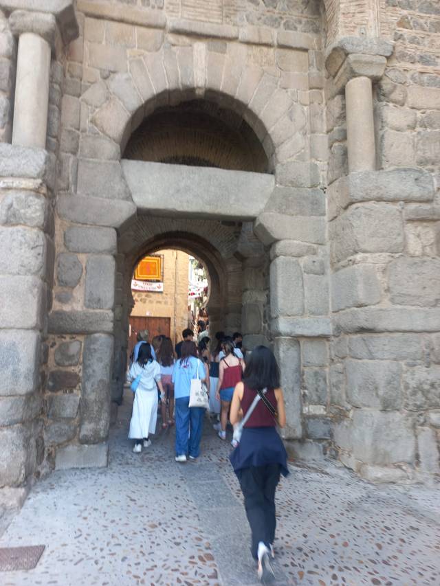 Grupo de personas caminando a través de un arco de piedra en una calle histórica.