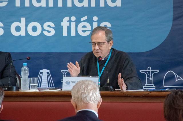 Un hombre habla en una mesa de conferencias frente a una audiencia en un evento.