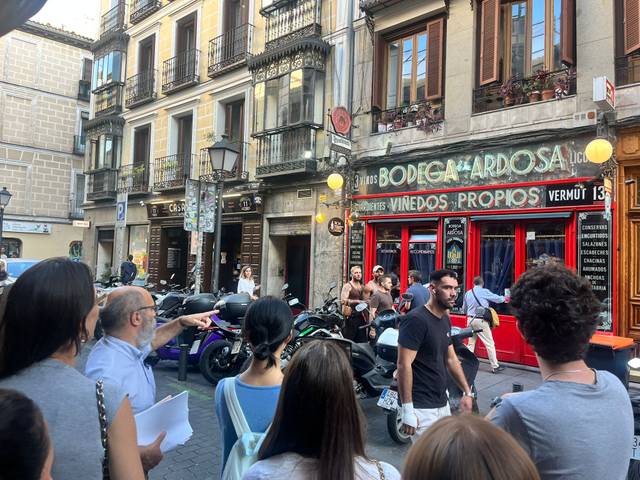 Una calle concurrida con motos estacionadas y personas conversando frente a un bar.