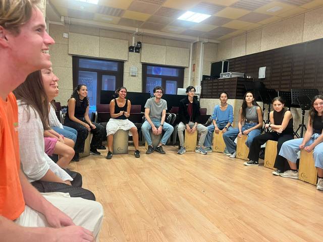 Un grupo de jóvenes sentados en círculo, participando en una actividad musical en un salón.