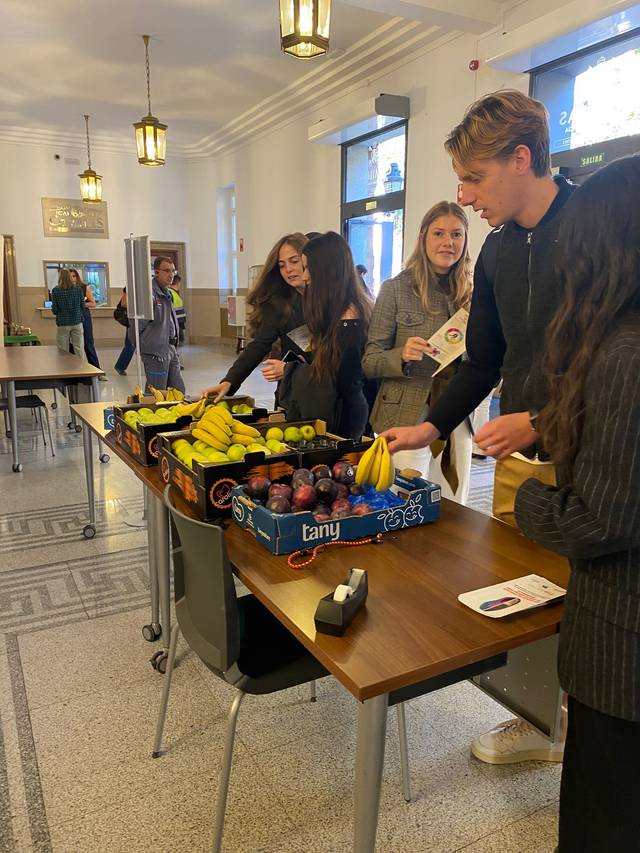 Un grupo de personas está eligiendo frutas en una mesa dentro de un edificio.