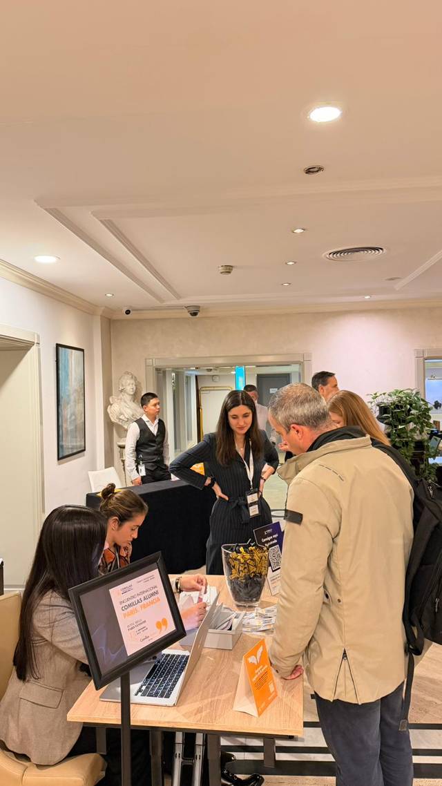 Una recepción con varias personas interactuando y un par de trabajadores atendiendo en un mostrador.