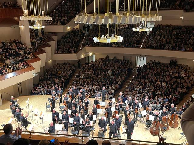 Una orquesta está presentando un concierto ante un público numeroso en un auditorio.