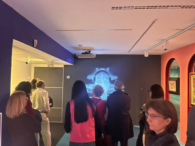 Un grupo de personas observa una proyección en la pared de una sala de exposición.