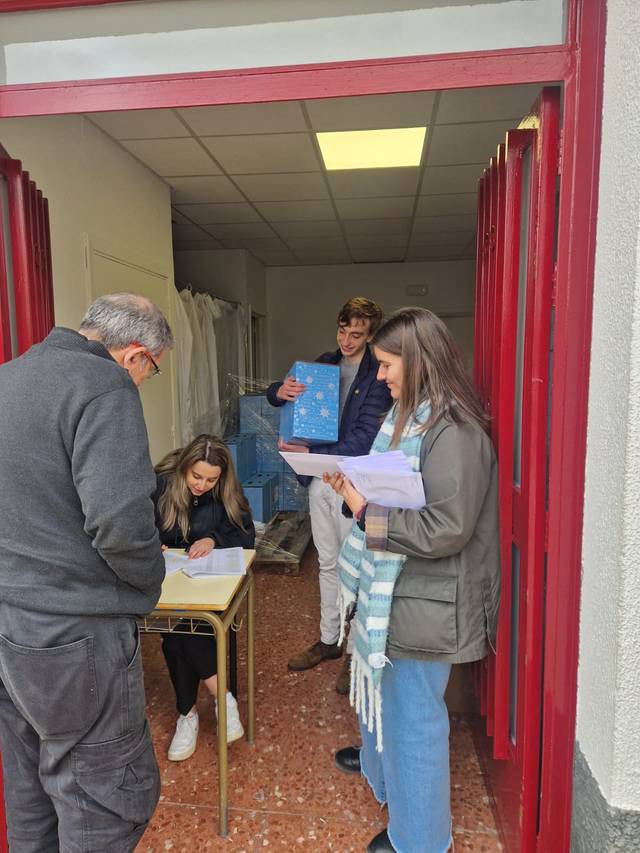 Un grupo de personas interactúa en la entrada de un local, con papeles en las manos.