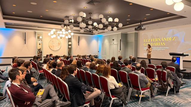Una conferencia con un presentador y una audiencia atenta en un salón con iluminación moderna.