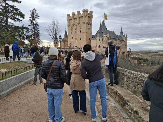 Un grupo de personas observa un castillo mientras pasean por un camino al aire libre.