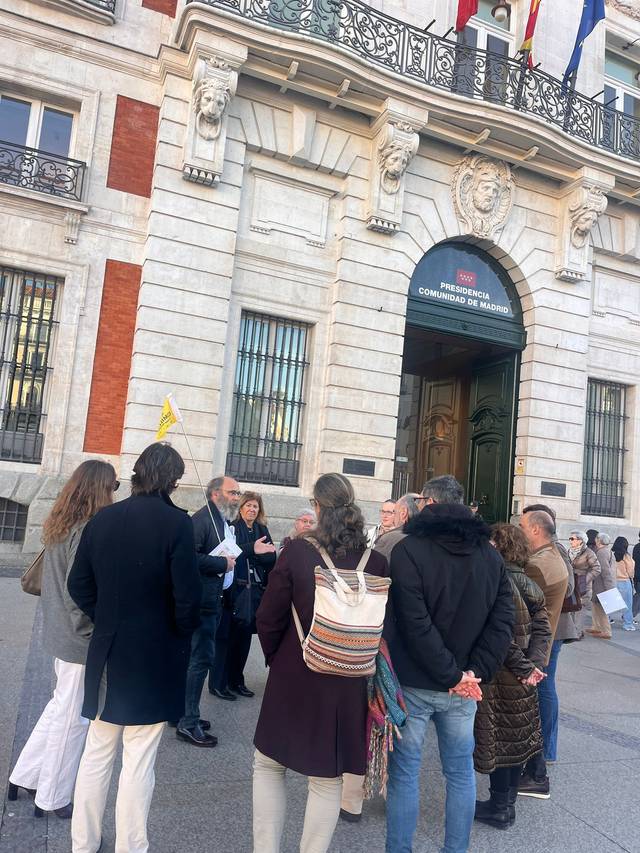 Un grupo de personas se reúne frente a un edificio histórico con banderas en la fachada.