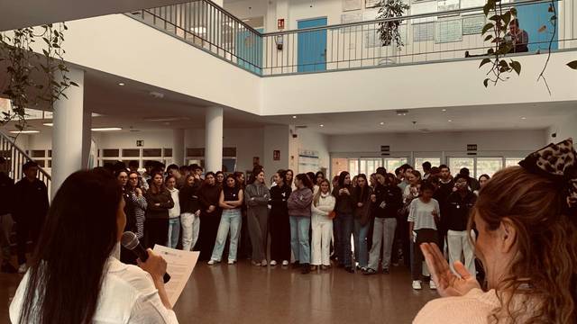 Un grupo de personas escucha atentamente a una oradora en un evento en un espacio cerrado.