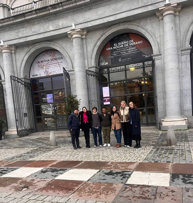 Un grupo de personas posando frente a un edificio con arcos y carteles de teatro.
