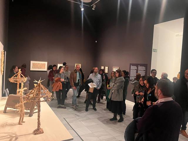 Una multitud observa una exposición de arte en una sala con paredes oscuras.