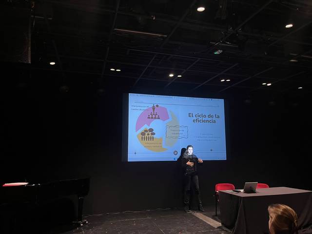 Una persona presenta un gráfico sobre el ciclo de la eficiencia en un escenario oscuro.