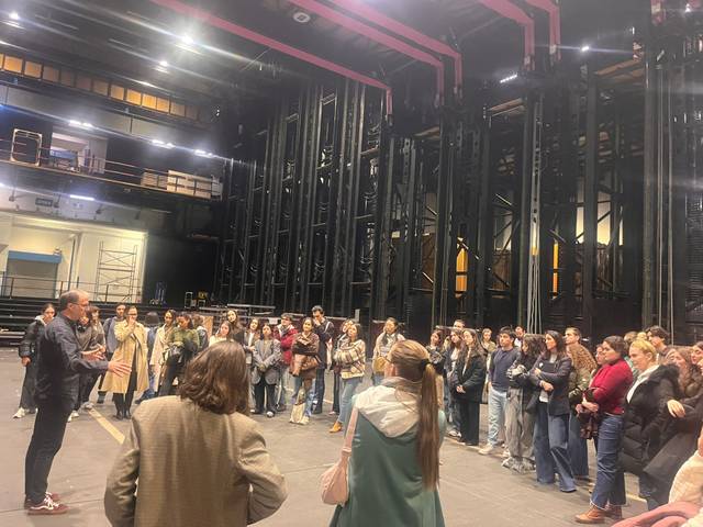 Un grupo grande de personas está reunido en un escenario de teatro con un orador al frente.