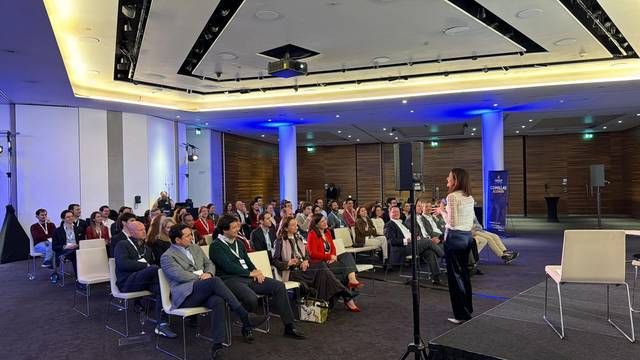 Una oradora presenta frente a una audiencia en un evento profesional.