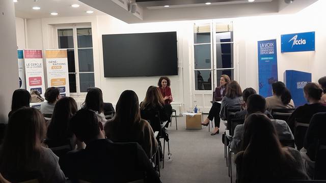 Una charla en un evento donde dos mujeres conversan frente a una audiencia sentada.