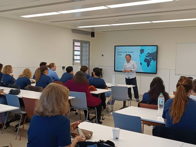 Una presentación en un aula con un ponente frente a un grupo de personas.