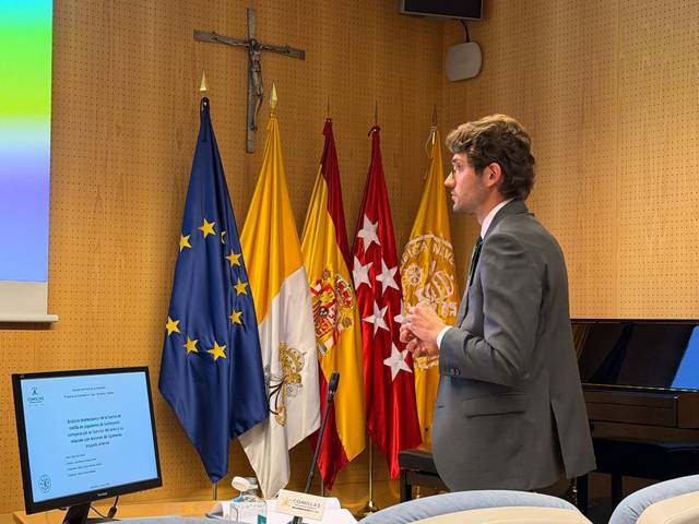 Un hombre está dando una presentación en una sala con banderas y un proyector.