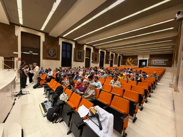Un grupo de personas asiste a un evento en una sala con asientos naranjas.