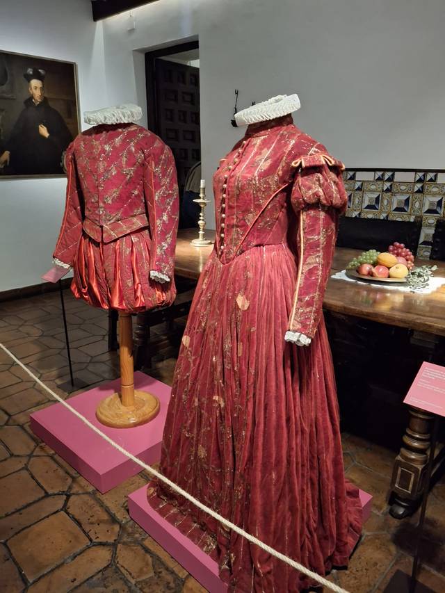 La imagen muestra dos trajes antiguos en tonos rojos exhibidos en un museo.