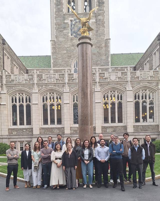 Un grupo de personas posando frente a un edificio con una columna y una estatua de un águila en la parte superior.