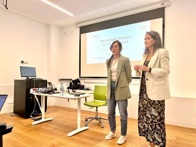 Dos mujeres están presentando un tema sobre aprendizaje de servicio en una sala de conferencia.