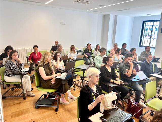 Un grupo de personas sentadas en una sala, trabajando en computadoras portátiles.