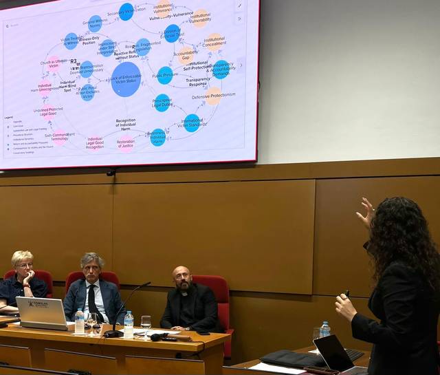 Una presentación en un evento con un gráfico en la pantalla y un ponente explicando a un público sentado.