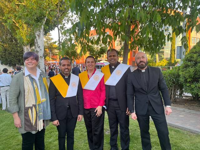 Un grupo de cinco personas posando juntas en un evento al aire libre, luciendo trajes formales y distintivos.