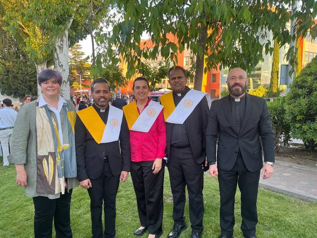 Un grupo de cinco personas vestidas formalmente posan para la foto al aire libre.