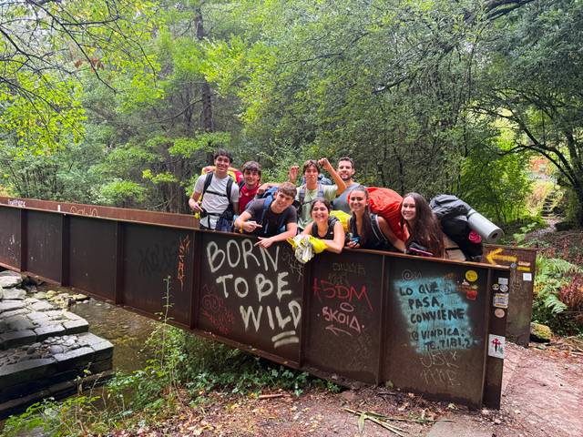Un grupo de jóvenes posa felices en un puente rodeado de naturaleza.