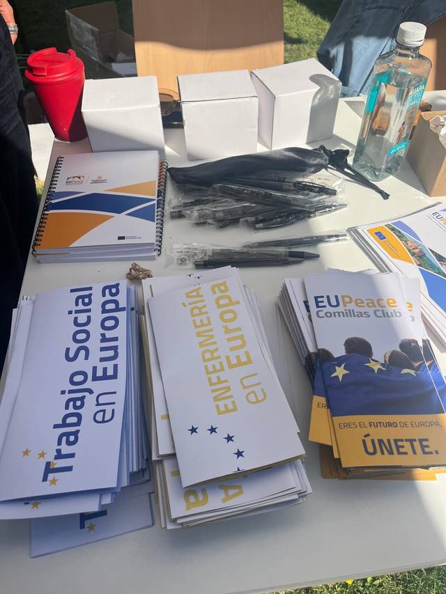 Mesa con folletos y materiales relacionados con programas europeos en un evento al aire libre.
