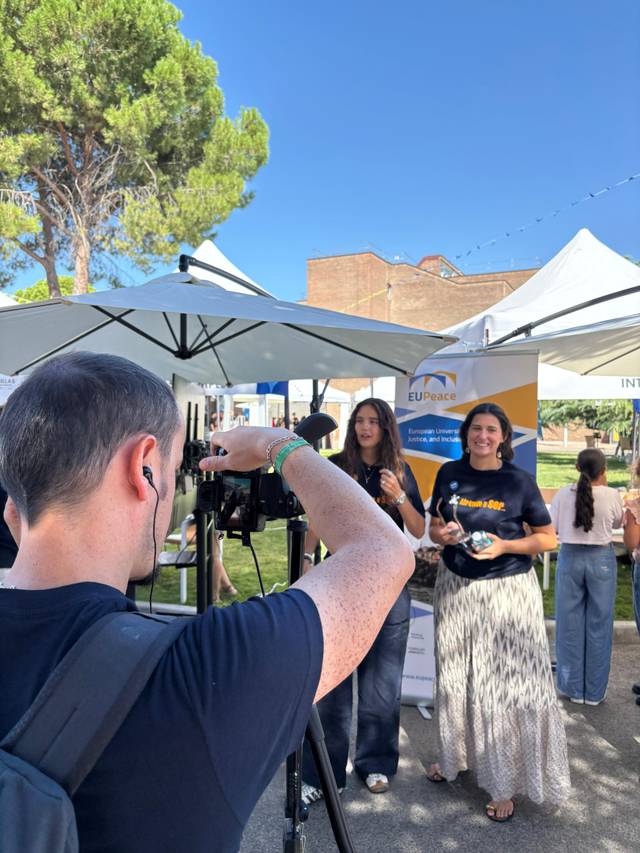Una persona está grabando a dos mujeres bajo una sombrilla en un evento al aire libre.