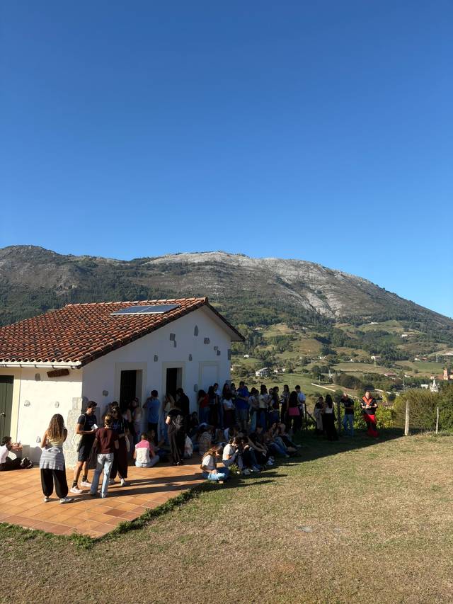 Un grupo de personas se reúne frente a una casa en un paisaje montañoso bajo un cielo despejado.