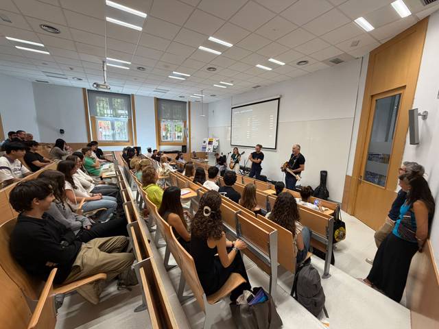 Un grupo de estudiantes asisten a una charla en un aula moderna con un ponente en el frente.